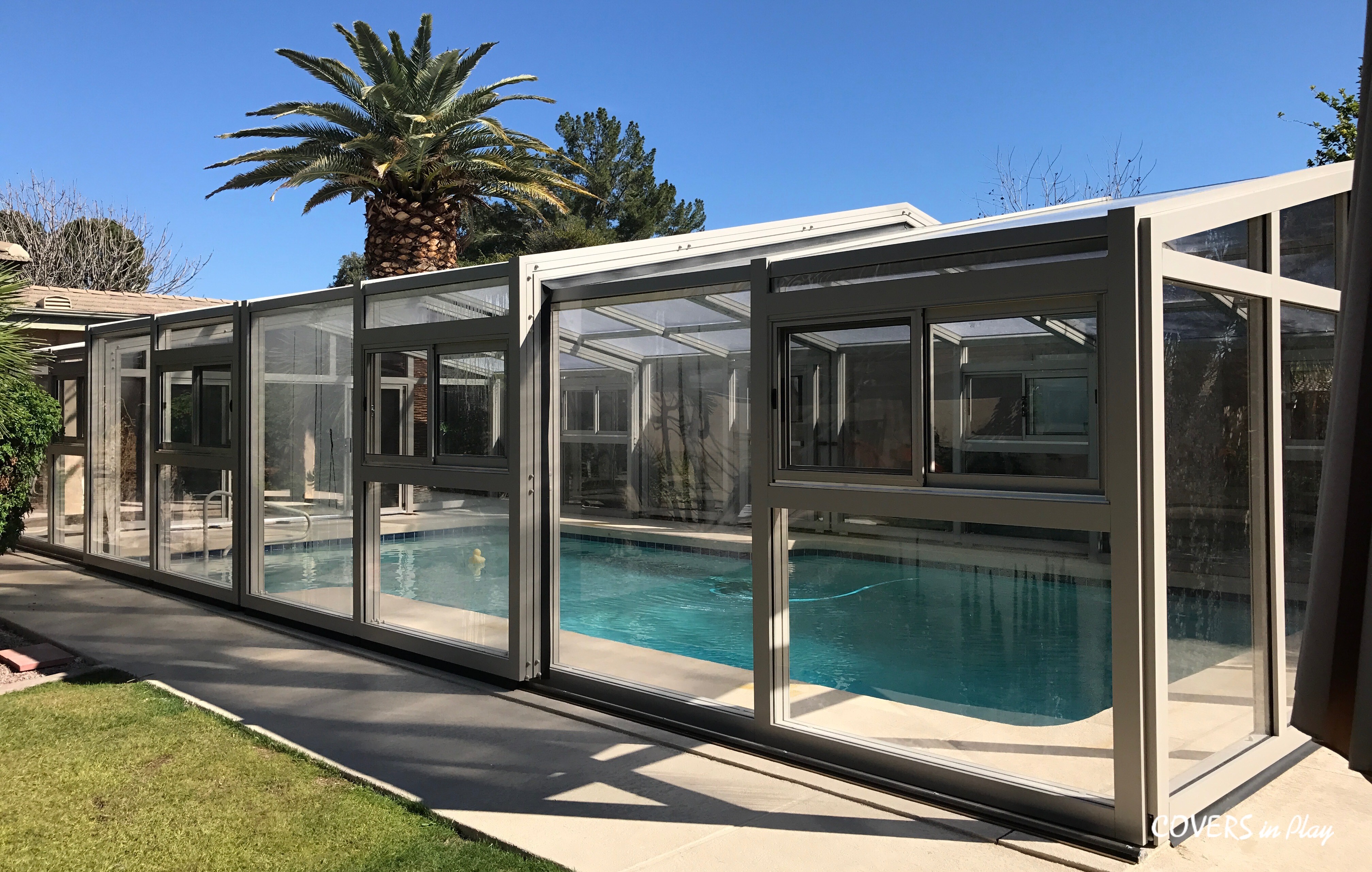 Glass swimming pool enclosure with sliding doors and clear panels surrounding an indoor residential pool