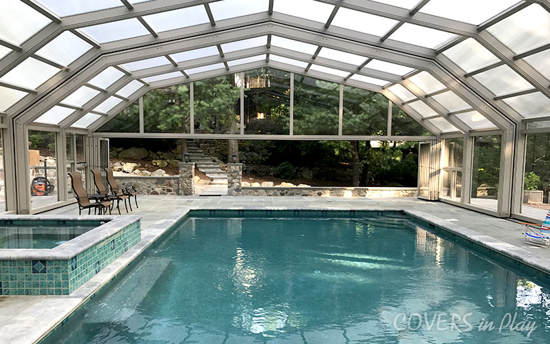 Interior view of pool dome cover in Kinnelon, NJ, featuring bi-fold doors and
            a stone walkway to the house.