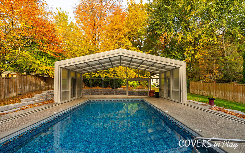 Exterior view of open pool dome cover in Whitby, ON, with lush autumn
            trees in the backyard.